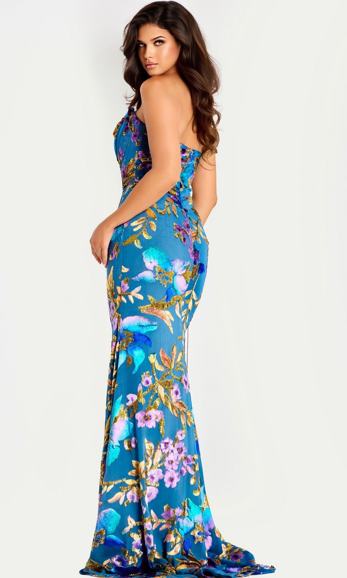 A woman models the Jovani 47654, a strapless blue long prom dress with a colorful floral pattern, standing sideways against a plain background.